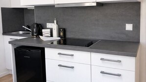 Moderni keittiö, jossa on valkoiset kaapit, musta astianpesukone ja harmaa työtaso.
