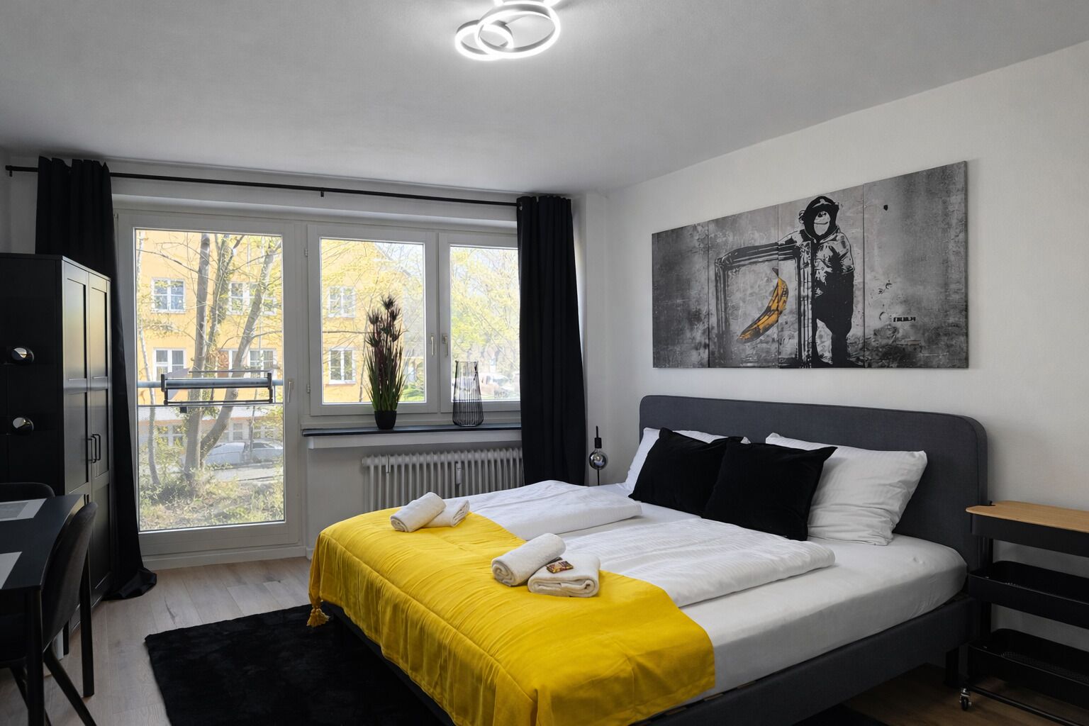 Une chambre à coucher avec un lit, un bureau, une chaise, une fenêtre et un tableau accroché au mur.