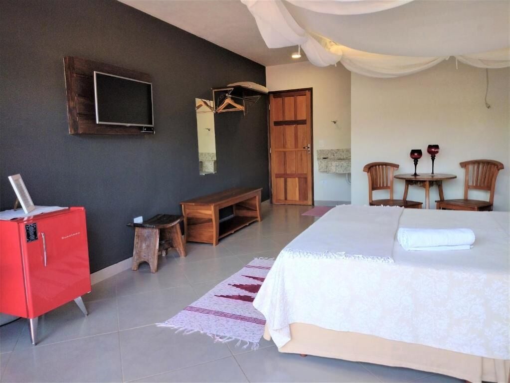 A bedroom with a bed, a TV mounted on the wall, a wooden bench, a red cabinet, and a small table with two wine glasses.