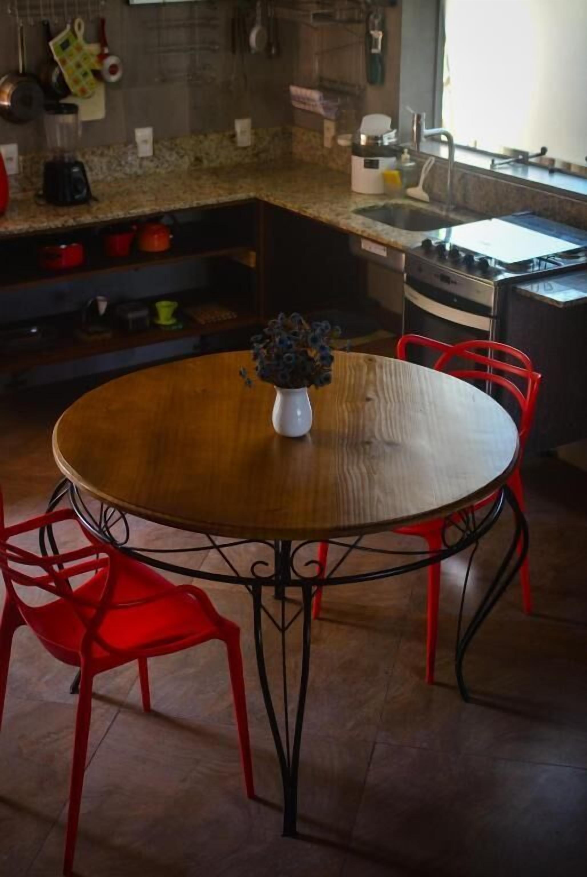 A kitchen with a round wooden table, red chairs, and a vase with flowers.