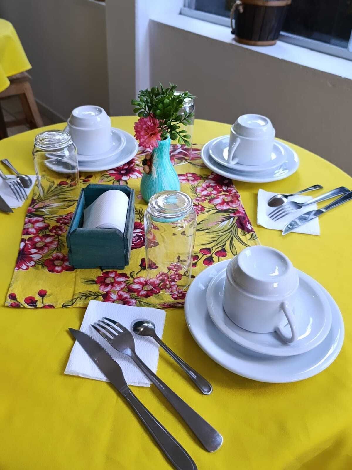 A table set with white dishes, silverware, and a floral tablecloth.