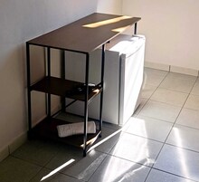 A corner kitchenette with a built-in fridge, a shelf unit, and a towel on the floor.