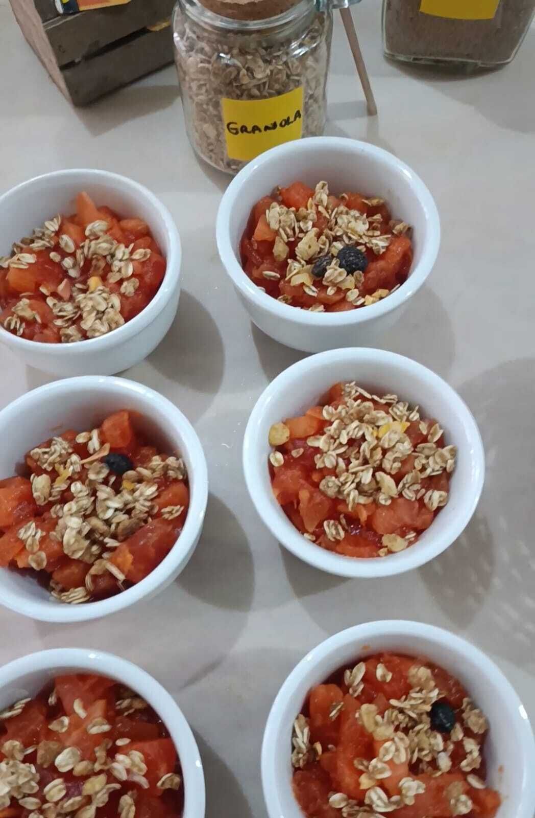 Seis tazones blancos con granola y fruta sobre una mesa.