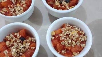 Seis tazones blancos con granola y fruta sobre una mesa.
