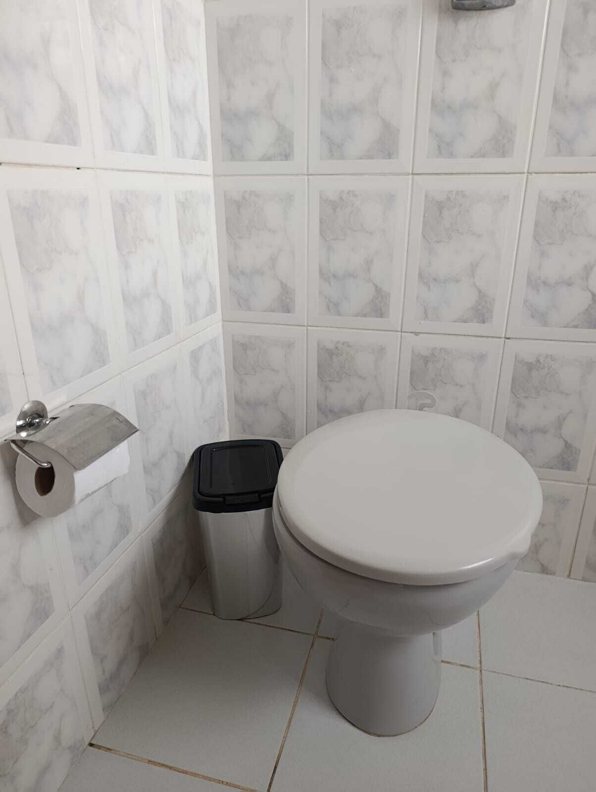 A bathroom with a toilet, a trash bin, and a toilet paper holder.
