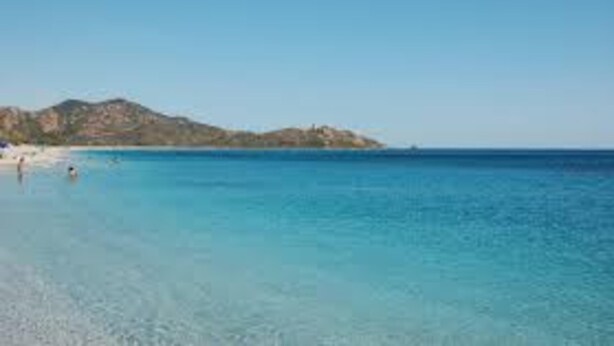 A beach with clear water, a mountain in the background, and a few people swimming. - Apartment 'Casa Nenna' with Air Conditioning (San Vito)