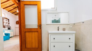 A bathroom with a wooden door, white sink, and a small trash bin. - Apartment 'Casa Nenna' with Air Conditioning (San Vito)