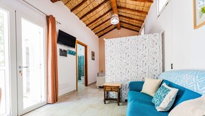 A room with a blue sofa, a wooden stool, a patterned curtain, and a television on the wall. - Apartment 'Casa Nenna' with Air Conditioning (San Vito)