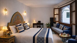 A hotel room with a large bed, a sofa, a small table, and decorative wall sconces. - Riad Symphony 808 (Fes)