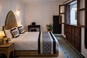 Quarto com cama grande, escrivaninha, planta em vaso e vista para o exterior.