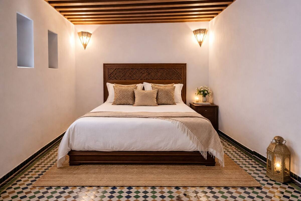 A bedroom with a large bed, two wall sconces, a nightstand with a lamp, and a decorative lantern.