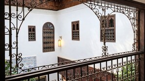 A balcony with ornate wrought iron railings, a white wall with decorative window grills, and a wooden staircase. - Riad Symphony 808 (Fes)