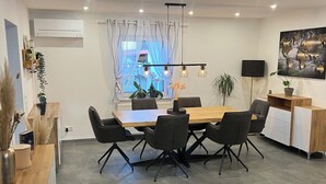 A modern dining area with a wooden table and black chairs, a grey sofa, and a small kitchen area with a white cabinet. - Andy's apartment (Malsch)