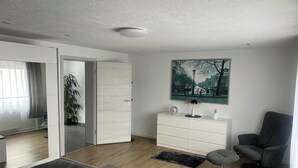 A modern living room with a sofa, a chair, a white cabinet, a painting, and a potted plant. - Andy's apartment (Malsch)