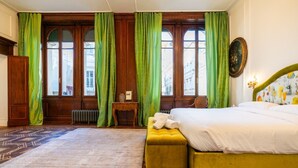 Ein Zimmer mit einem Bett, einem Heizkörper, einem kleinen Tisch und einem Fenster mit grünen Vorhängen.