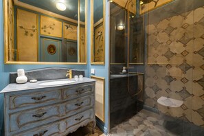 Ein Badezimmer mit Marmorbecken, einem Badezimmerhocker im Vintage-Stil und einer Duschkabine.
