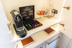 Eine Kaffeemaschine, eine Schokoladentafel und eine Glaskomposition mit Pralinen auf einer weißen Arbeitsplatte.