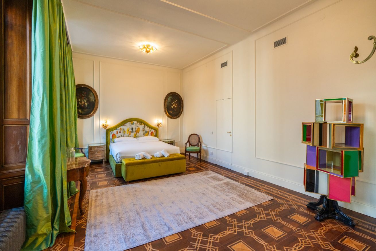 A bedroom with a bed, a chair, a bedside table, a mirror, and a decorative shelf.