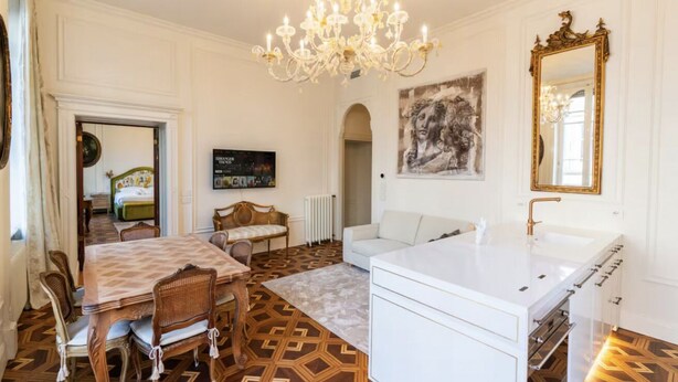 Ein Zimmer mit Esstisch, Stühlen, einer Couch, einem weißen Waschbecken, einer Kristallleuchter, einem Gemälde und einem Spiegel.