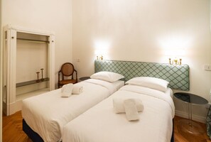 Ein Hotelzimmer mit zwei Betten, einem Schrank, einem Sessel und Nachttischlampen.
