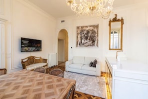A room with a dining table, a sofa, a chandelier, a framed artwork, and a television. - Catullus: A Noble and Imperial Residence   (Verona)