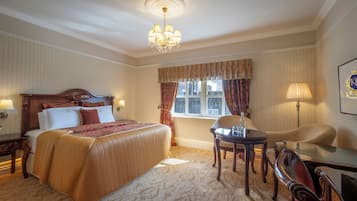 A hotel room with a large bed, a chandelier, a window with curtains, a desk, and a chair.