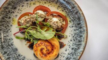 Un plato de comida con diversos ingredientes, incluyendo tomates, verduras de hoja y un elemento redondo que parece ser queso o huevo.