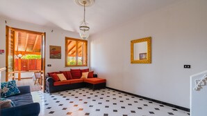 Un soggiorno con pavimento a scacchi bianco e nero, un divano nero con cuscini rossi, un divano blu con un cuscino floreale e un soffitto in legno.