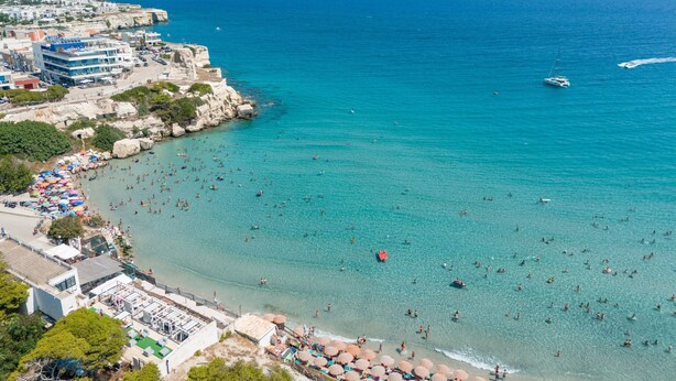 Vista aerea di una zona costiera con spiaggia, acque blu cristalline e un litorale roccioso.