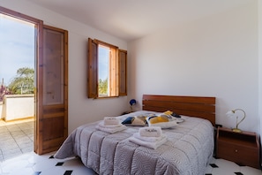 Ein Schlafzimmer mit einem Bett, zwei geöffneten Türen, einem Nachttisch und einem Fenster.