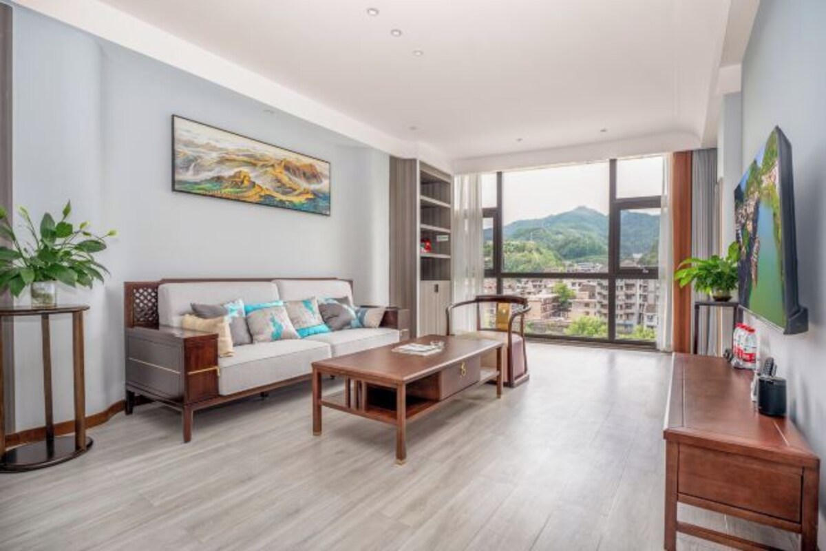 A modern living room with a sofa, coffee table, and a large window offering a view of a mountainous landscape.