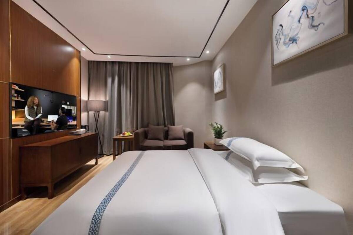 A hotel room with a large bed, a desk with a computer, a sofa, a lamp, and a painting on the wall.