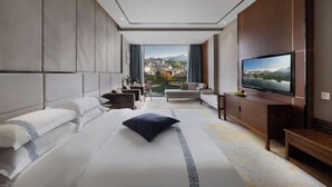 A modern hotel room with a large bed, a television, and a view of a cityscape.
