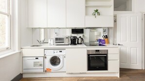 Uma cozinha compacta com armários brancos, máquina de lavar embutida, micro-ondas, cafeteira e forno pequeno.