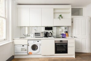 A compact kitchen with white cabinetry, a built-in washing machine, a microwave, a coffee maker, and a small oven. - New! Central 1BR, steps to Soho, Oxford St (Greater London)