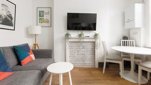 Uma sala de estar moderna com um sofá cinzento, uma mesa redonda branca, uma TV montada acima de uma lareira e um armário branco.