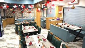 A restaurant with booths and tables, some with red napkins and white plates. - Hotel Aaradhya inn (Dwarka)