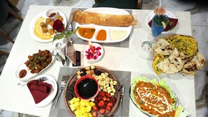 A table with various dishes including a rolled flatbread, a bowl of curry, and a plate with sliced bananas and strawberries. - Hotel Aaradhya inn (Dwarka)