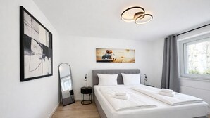 Ein modernes Schlafzimmer mit einem Bett, einem Nachttisch, einem Spiegel, einem Gemälde und einem Fenster mit Vorhängen.