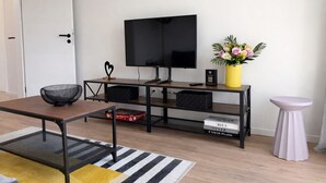 Ein modernes Wohnzimmer mit Fernseher, kleinem Tisch, Sofa, Couchtisch, Beistelltisch und einer dekorativen Vase.