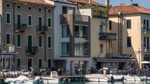 A waterfront building with balconies, a marina with boats, and a clear sky. - Palazzo Cordigero (Peschiera del Garda)