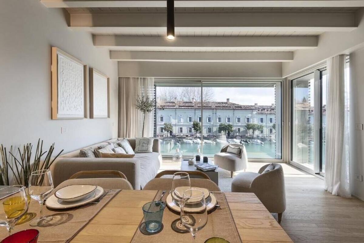 A modern living room with a dining area, large windows, and a view of a pool and buildings.