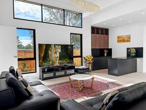 A modern living room with a large flat-screen TV, black leather sofas, a round coffee table, and a decorative rug. - Sereno - Fabulous golf resort getaway (POKOLBIN)