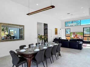 A modern dining area with a large table set for six, a dark-colored sofa, and a large mirror on the wall. - Sereno - Fabulous golf resort getaway (POKOLBIN)