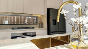 Een moderne keuken met een roestvrijstalen koelkast, een gasfornuis en een gouden kraan.