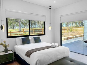 A modern bedroom with a large bed, a view of a fenced outdoor area, and a small bedside table with a vase. - Sereno - Fabulous golf resort getaway (POKOLBIN)