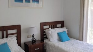 A hotel room with two beds, a nightstand with a lamp, a framed picture on the wall, and a window with curtains. - 3-bedroom villa in peaceful  Roda Golf with AC (San Javier)