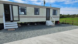 Uma casa móvel com varanda frontal, escadas e entrada por um caminho de cascalho.
