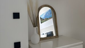 Ein weißer Schminktisch mit Spiegel, ein Kleiderständer aus Holz und eine Vase mit Trockenpflanzen.