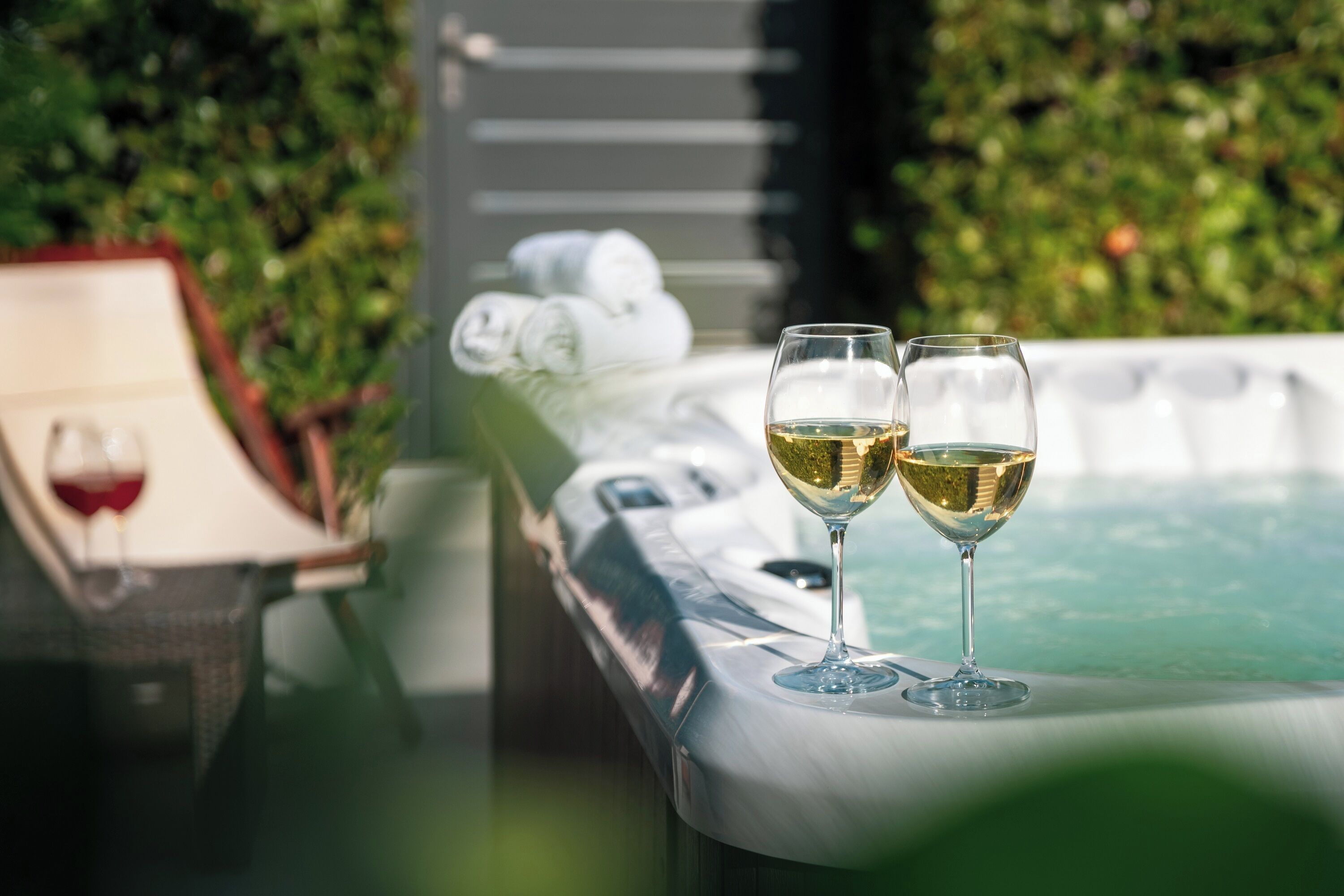 A hot tub with two glasses of white wine, a framed picture, and towels.
